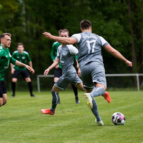 Zwei Fu&szlig;ballmannschaften spielen auf einem gr&uuml;nen Rasenplatz; ein Spieler in Grau dribbelt den Ball.