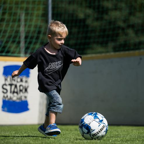 Junge in sportlichem Outfit dribbelt einen Fu&szlig;ball auf einem gr&uuml;nen Kunstrasenplatz.