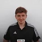 Junger Mann mit braunen Haaren, tr&auml;gt ein schwarzes Sporttrikot mit wei&szlig;en Streifen, vor einer hellen Wand.