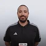 Portr&auml;t eines Mannes mit Bart in einem schwarzen T-Shirt mit wei&szlig;en Streifen, vor einem neutralen Hintergrund.