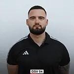 Portr&auml;t eines Mannes mit Bart, in schwarzem Sportshirt, vor neutralem Hintergrund, mit ernster Miene.