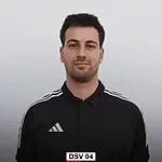 Junger Mann mit dunklem Haar und Adidas-Shirt, vor neutralem Hintergrund stehend, Blick zur Kamera.