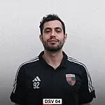 Portr&auml;t eines Mannes in schwarzem Sportshirt mit Vereinslogo, vor neutralem Hintergrund, mit ernstem Gesichtsausdruck.