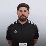 Portr&auml;t eines Mannes mit Bart, in schwarzem Trainingsanzug mit wei&szlig;en Streifen, neutraler Hintergrund.