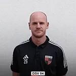 Portr&auml;t eines Mannes mit glattem Kopf, tr&auml;gt ein schwarzes Sporttrikot mit roten und wei&szlig;en Details.