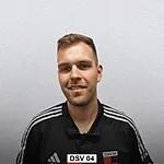 Portr&auml;t eines l&auml;chelnden Mannes in schwarzer Sportbekleidung mit Streifen, vor einem hellen Hintergrund.