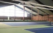 Sporthalle mit mehreren Tennispl&auml;tzen in Gr&uuml;n und Blau, helle Fenster sorgen f&uuml;r nat&uuml;rliche Beleuchtung.