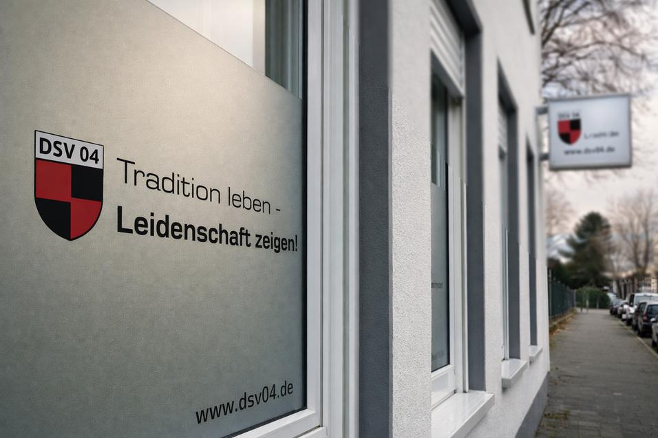 Fenster mit Schriftzug &bdquo;Tradition leben - Leidenschaft zeigen!&ldquo; an einem hellen Geb&auml;ude, Stra&szlig;enszene im Hintergrund.