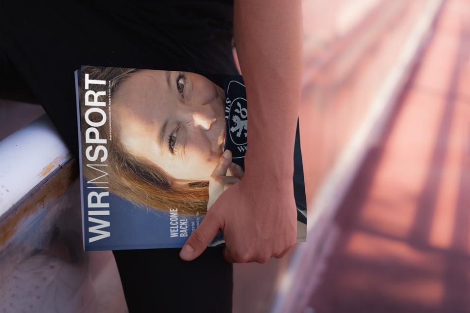 Eine Person h&auml;lt ein Magazin mit dem Titel &bdquo;WIR SPORT&ldquo; und blickt l&auml;chelnd in die Kamera.