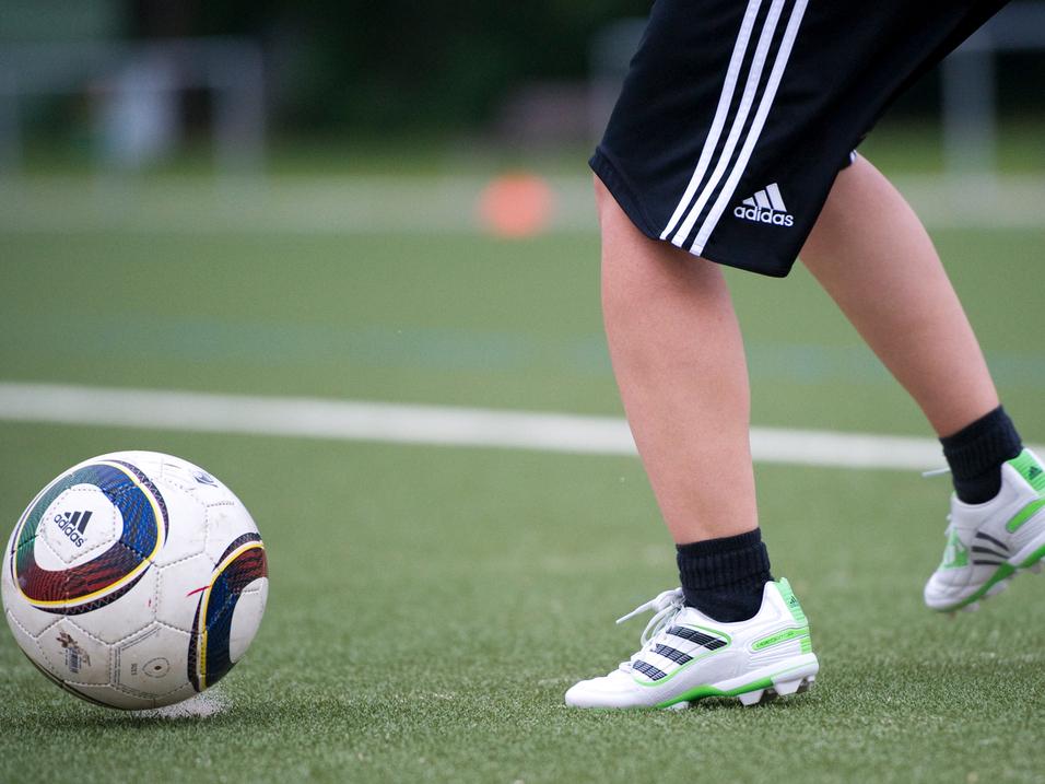 Ein Fuß mit Fußballschuhen tritt auf einen Fußball auf einem Kunstrasenfeld.
