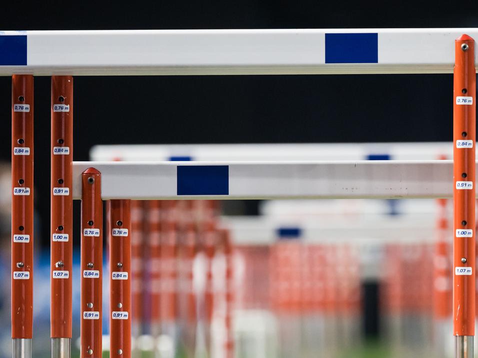 Reihe von Hürden auf einem grünen Sportfeld, mit unterschiedlichen Höhenangaben auf den Hürdenstangen.