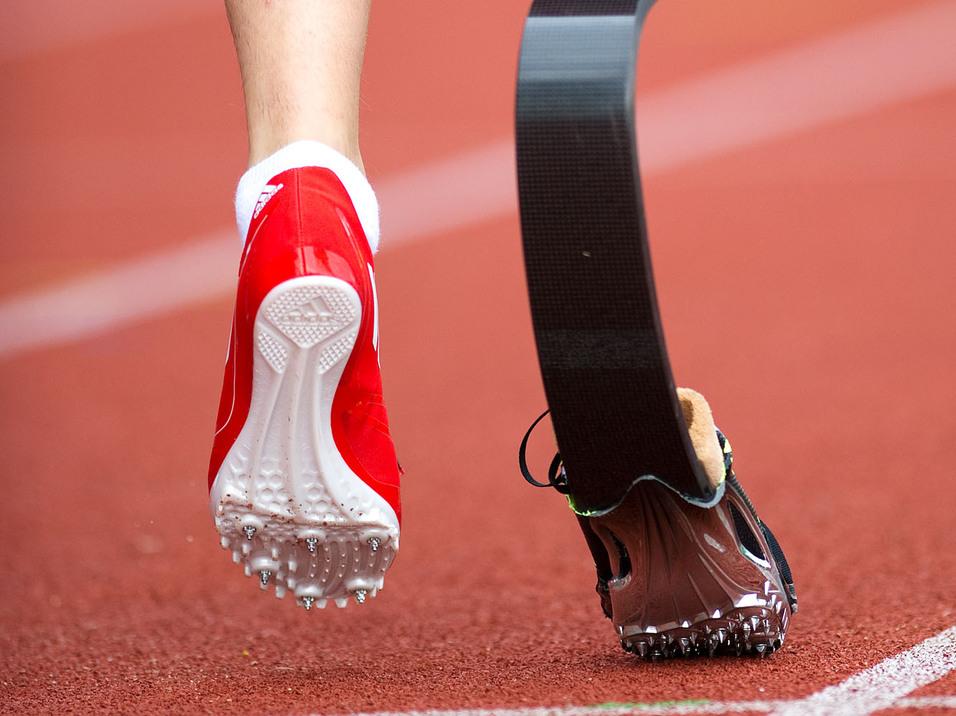 Fuß eines Läufers mit Prothese und rotem Schuh auf einer roten Laufbahn.