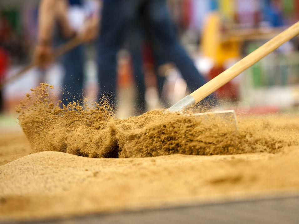 Arbeiter bearbeitet Sand mit einer Schaufel auf einem Sportplatz während einer Veranstaltung.