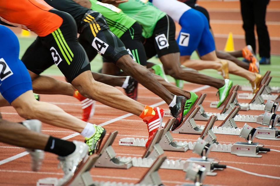 Start einer Sprintveranstaltung mit mehreren Athleten in Blockstartposition auf einer Laufbahn.